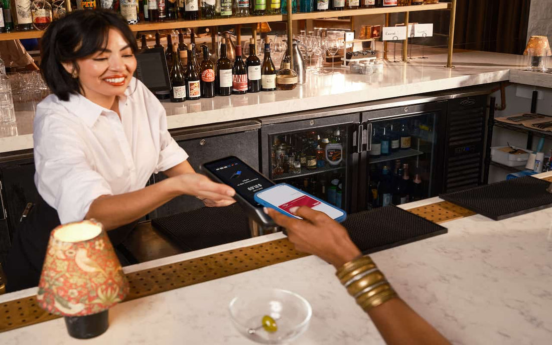 Gen Z customer silently using tap-to-pay phone at bar while bartender waits